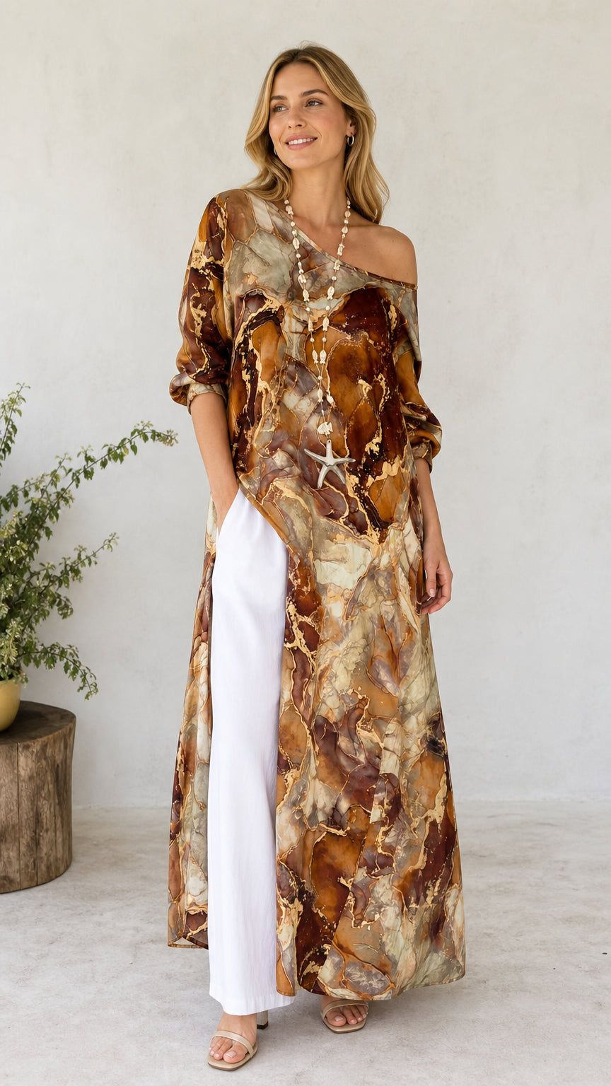 Front view of model wearing brown marble print off-shoulder maxi tunic dress with white pants