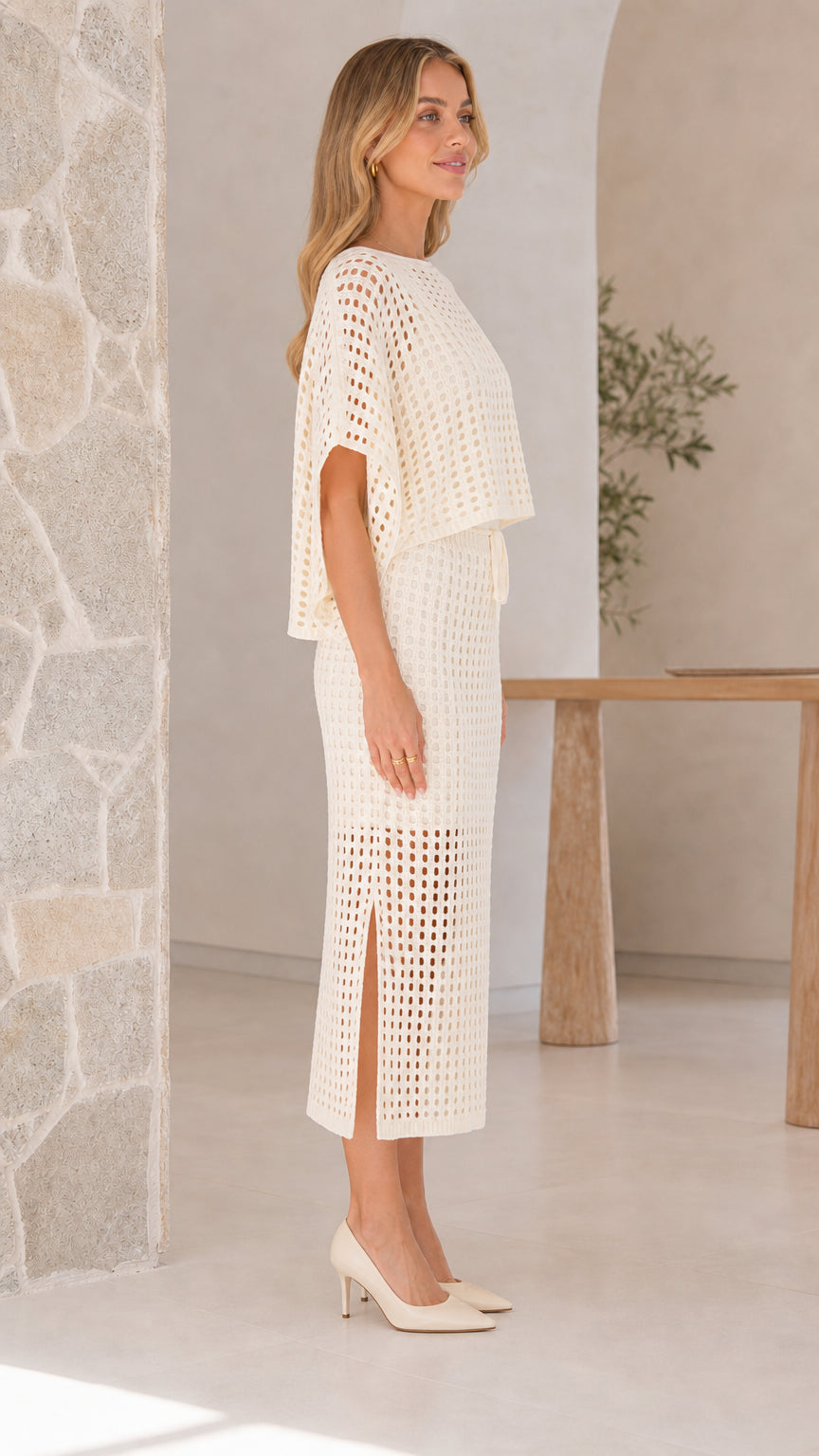 Model wearing off-white open-knit two piece skirt set, side view showing slit