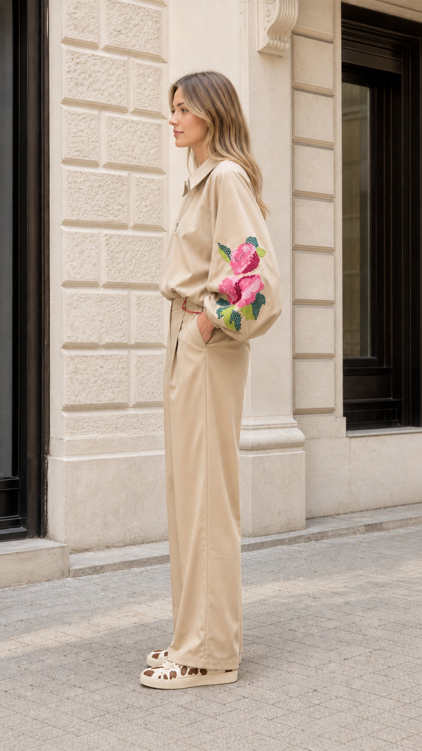 Side profile view of model in beige zip-up embroidered jacket and matching pleated trousers