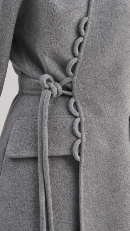 Close-up of the gray wrap coat's decorative loop buttons, waist tie, and flap pocket