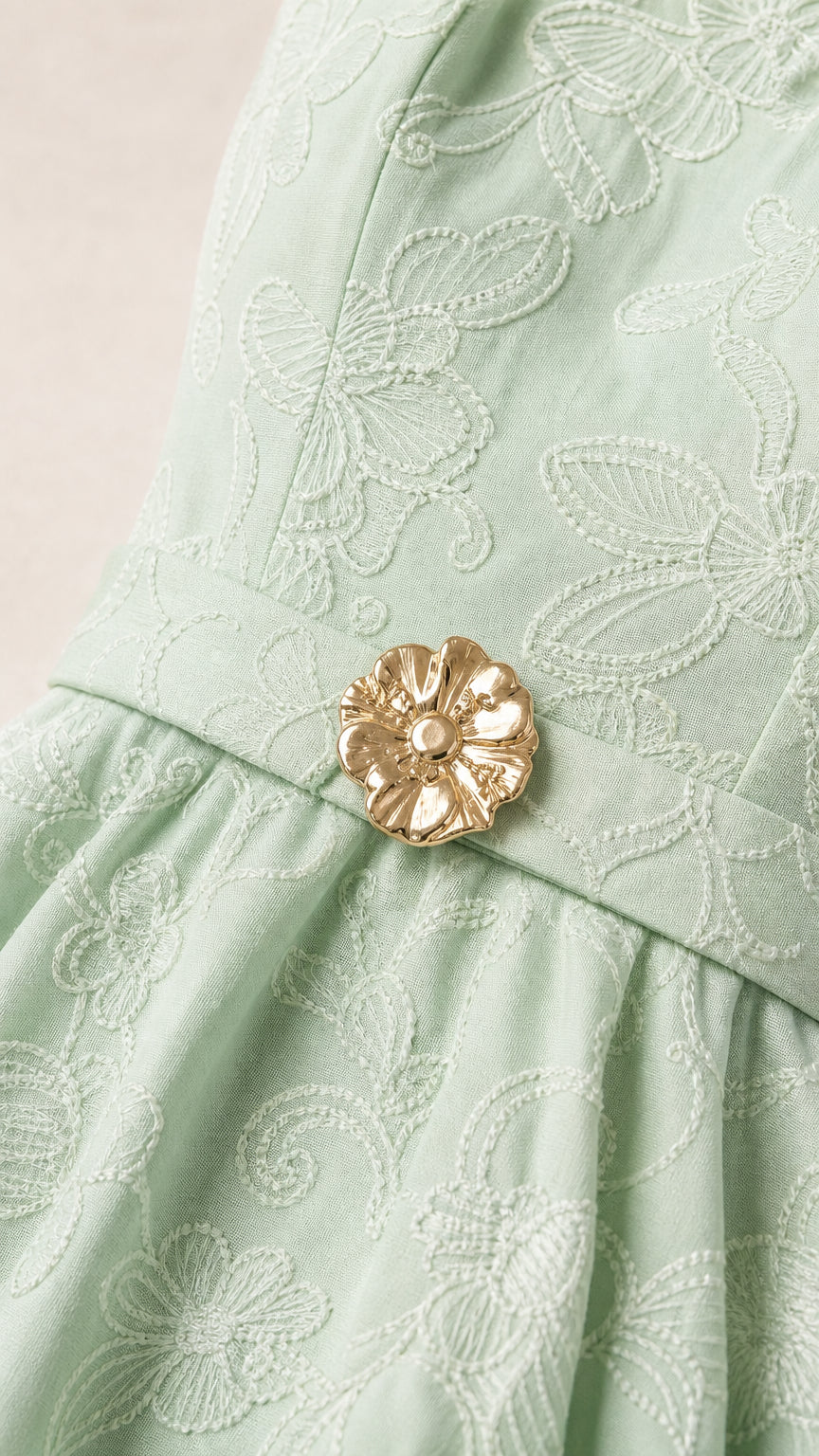 Close-up of mint green floral embroidery and gold flower belt buckle