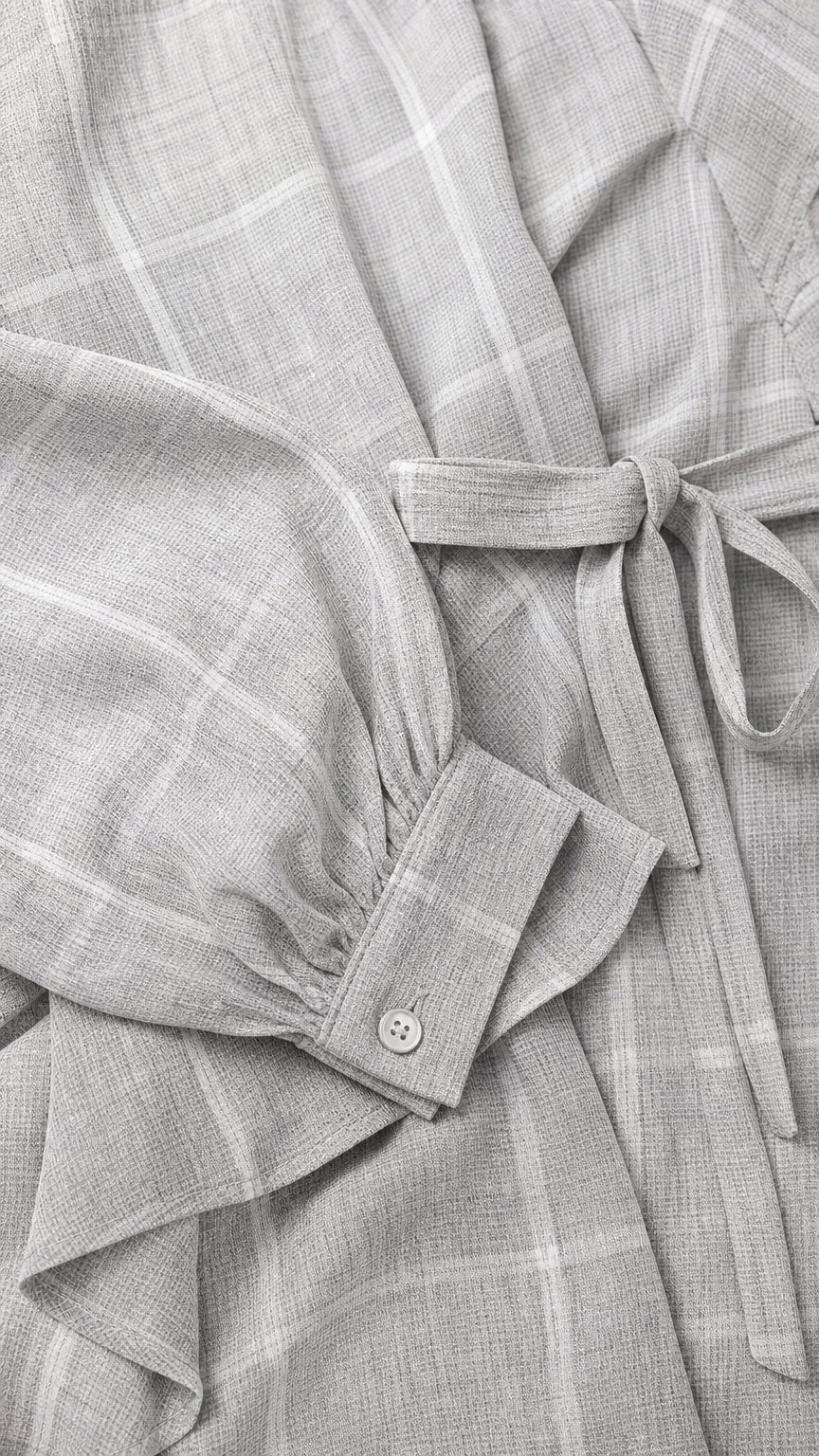 Close-up detail of sleeve cuff, buttons, and tie belt on light grey jumpsuit