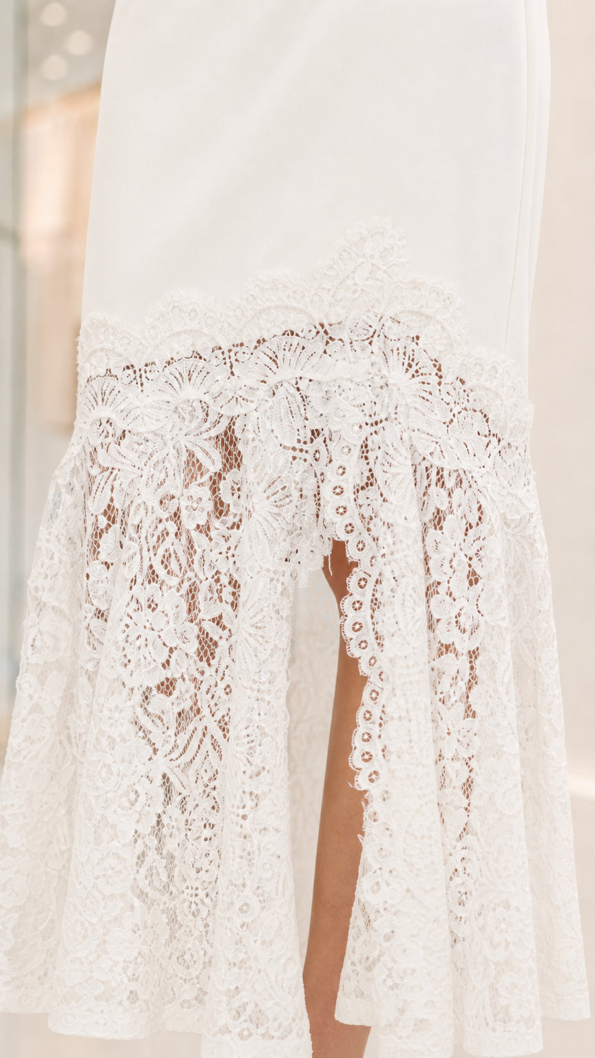 Close up view of the intricate white sheer floral lace hem with side split detail