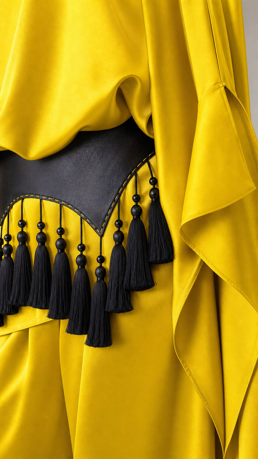 Close-up detail of black leatherette belt with beaded fringe tassels on yellow fabric