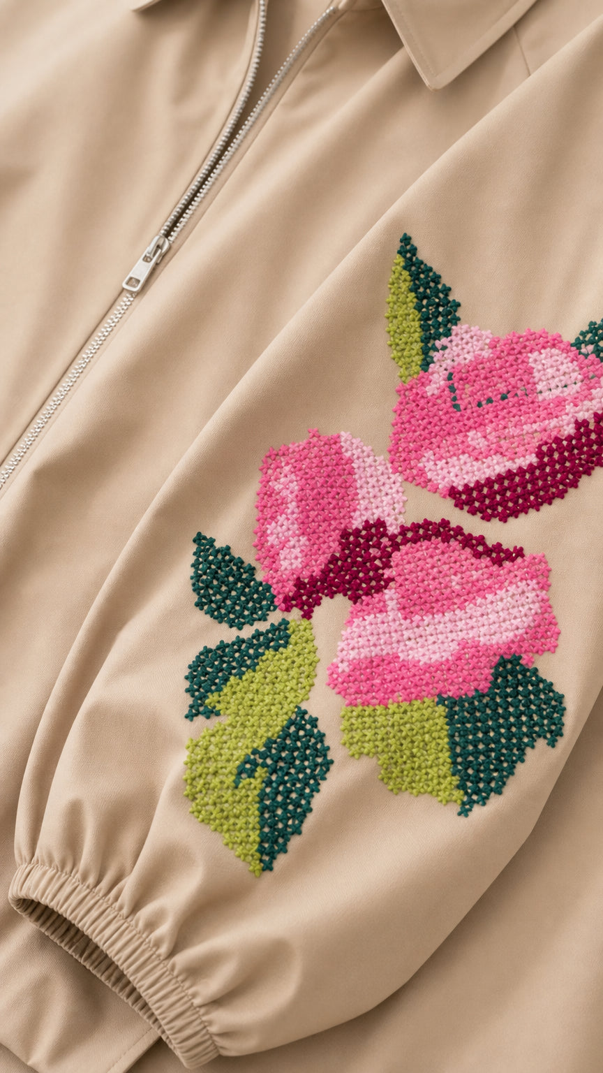Close-up detail of cross-stitch pink rose and green leaf embroidery on the beige jacket sleeve