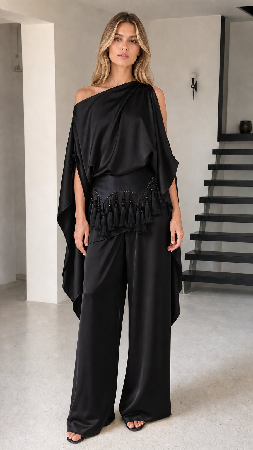 Model wearing black one-shoulder draped cape top and wide-leg pants set