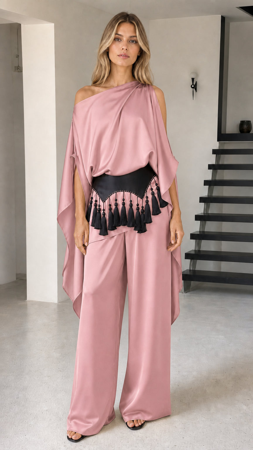 Model wearing dusty pink one-shoulder cape pant set with black tassel belt