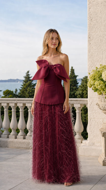 Front view of model wearing burgundy color variant of the bow corset and feather skirt set