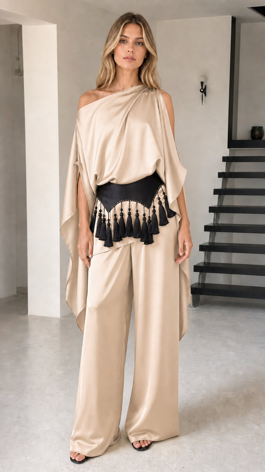 Model wearing champagne beige one-shoulder draped pant set with black tassel belt